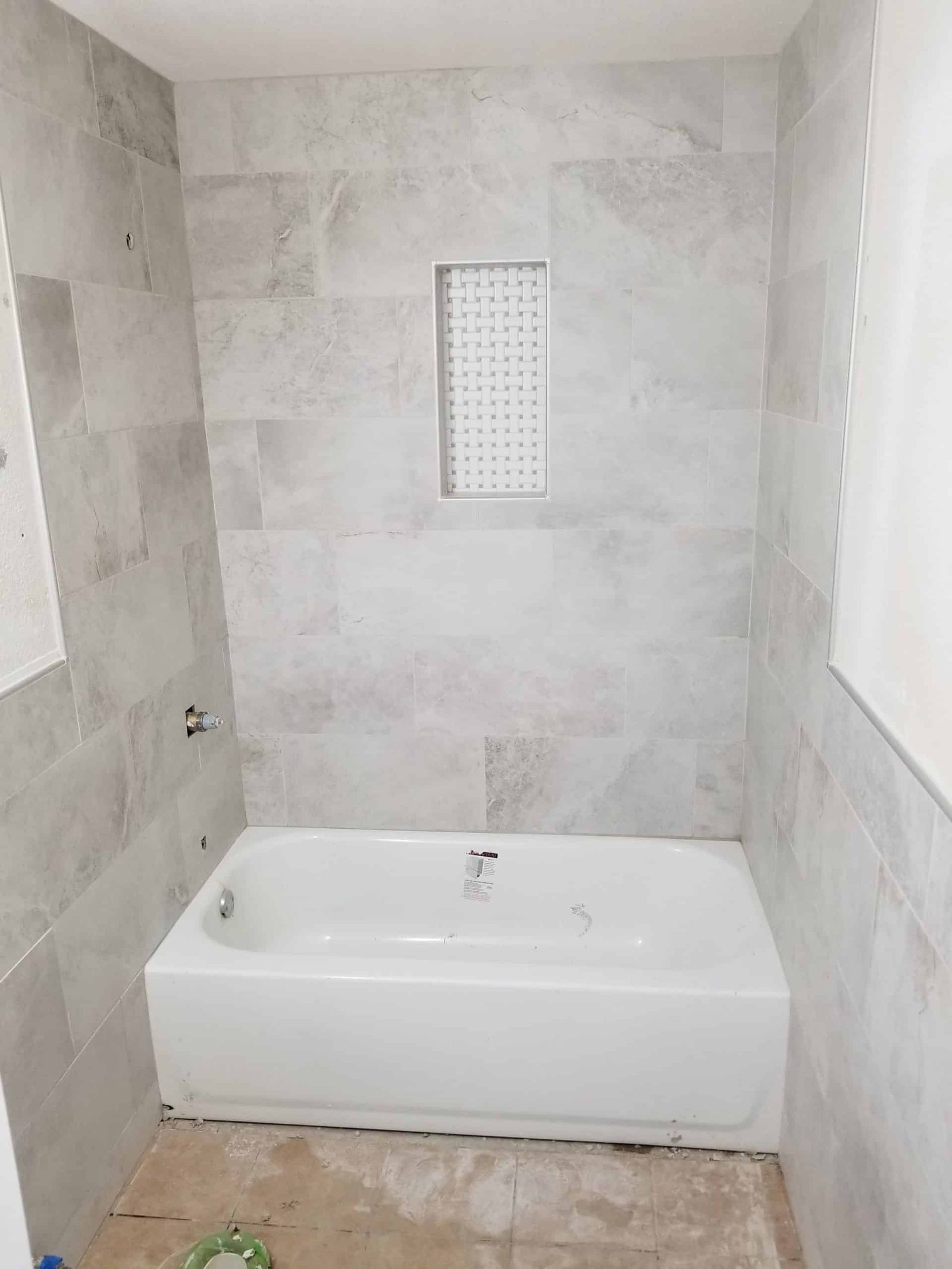 After: Gray tile tub surround with mosaic niche, plumbing unfinished
