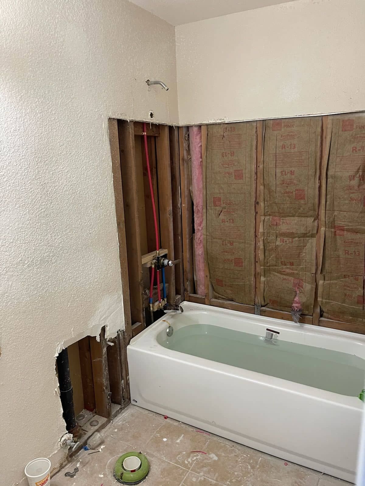 Before: Demolished bathtub surround with exposed insulation and plumbing