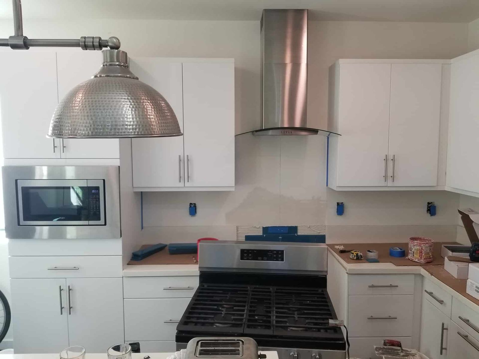 Before: Kitchen with white cabinets, stainless range hood, backsplash in progress