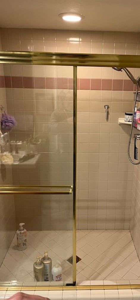 Before: Glass shower door with beige tile and pink accent stripe