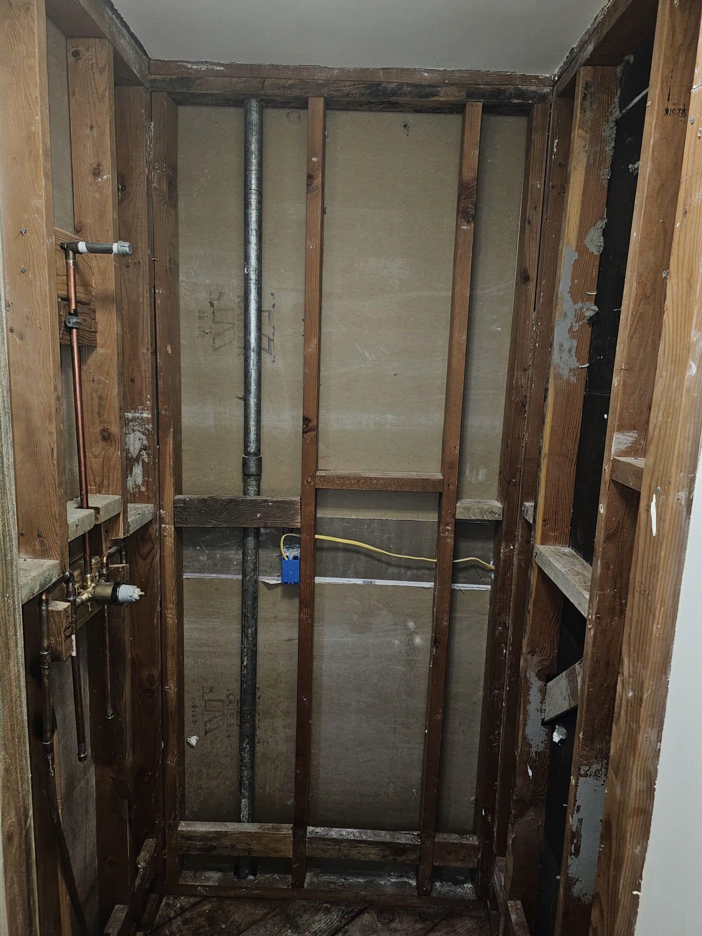 Before: Shower stall stripped to studs with exposed plumbing pipes