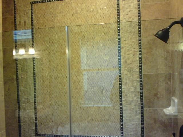 Glass shower door with mosaic tile walls and dark border trim