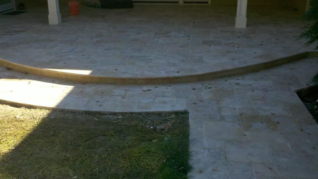 Curved travertine tile patio with edging under covered porch