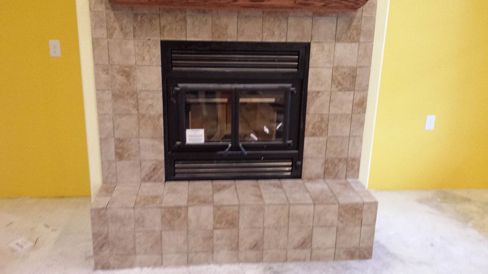 Beige tile fireplace surround with black insert and wood mantel