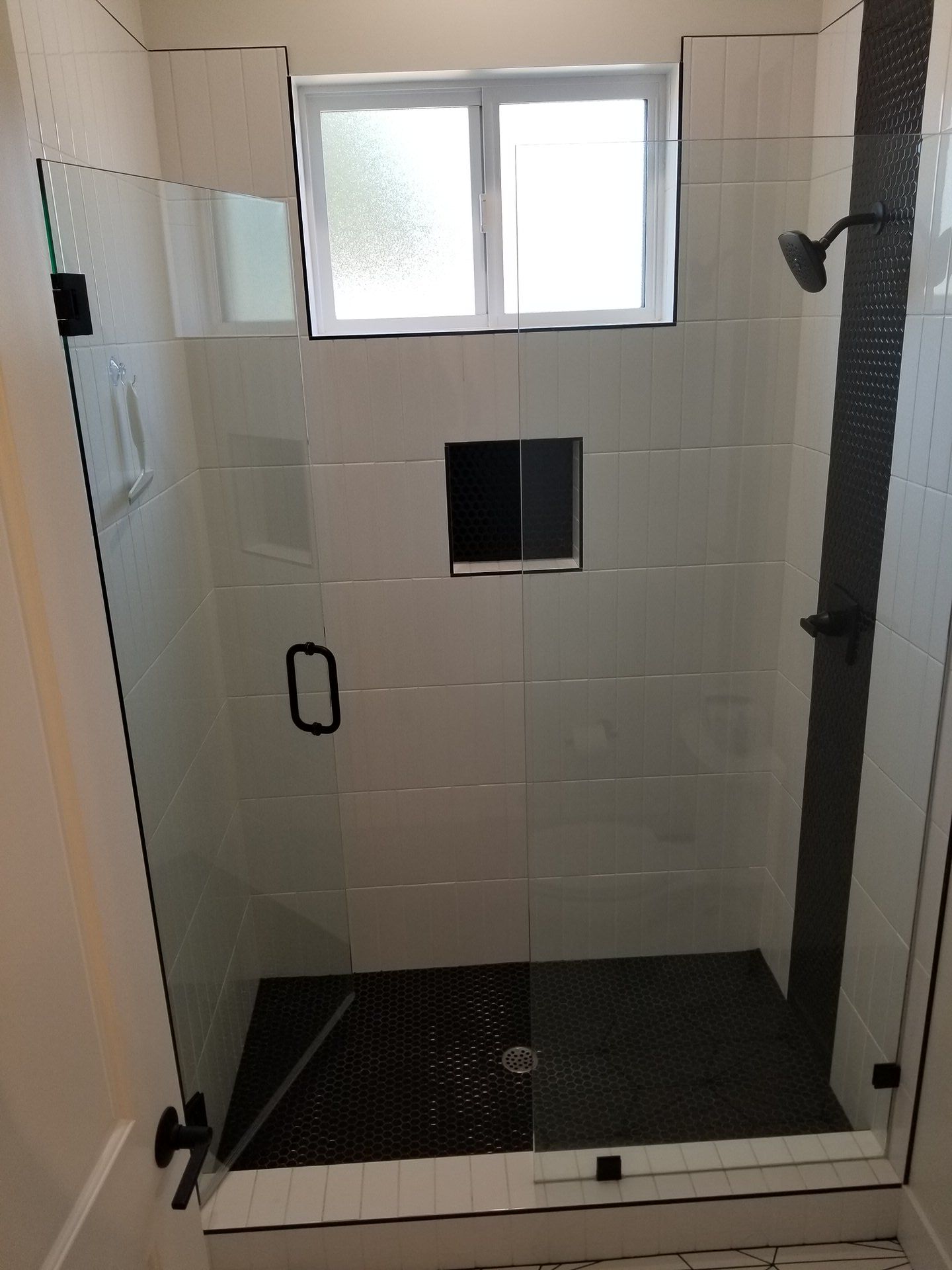 Glass shower enclosure with white subway tile and black hexagon niche and floor