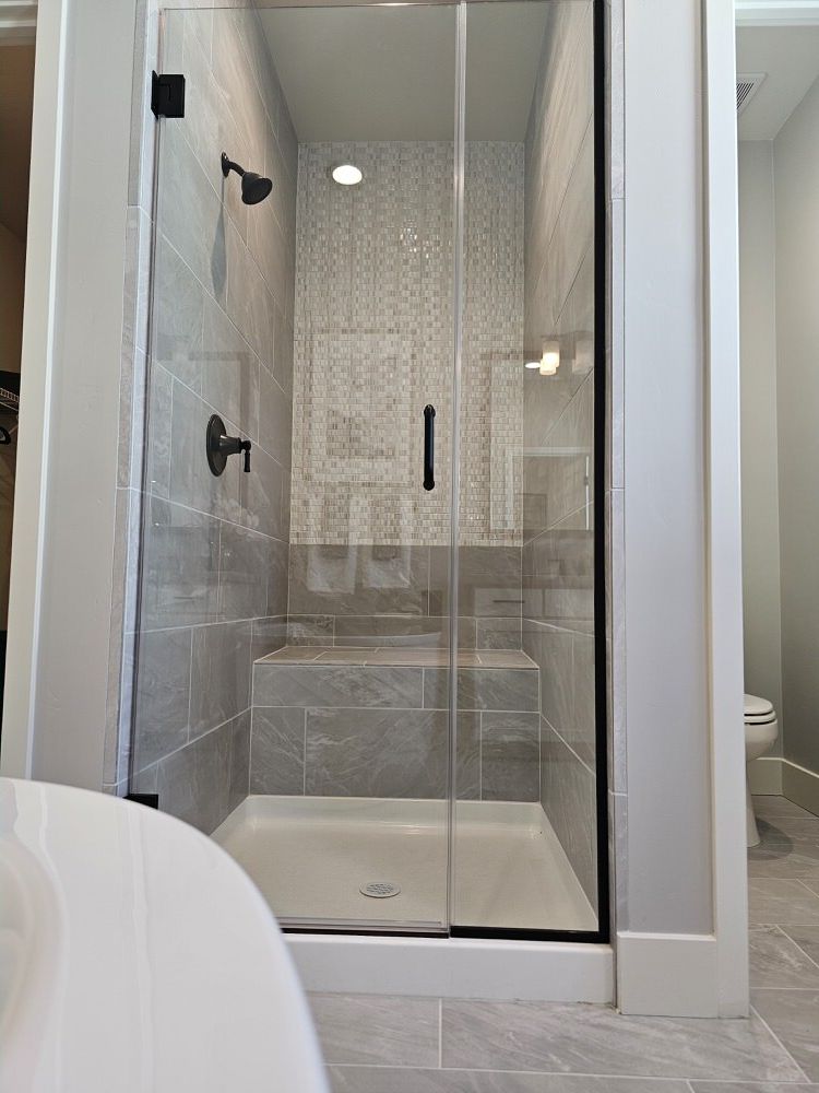 Glass enclosed shower with mosaic accent wall and tile bench