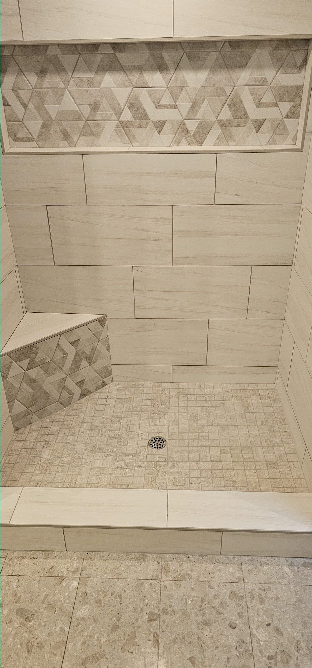 Tiled shower with geometric mosaic niche and corner bench
