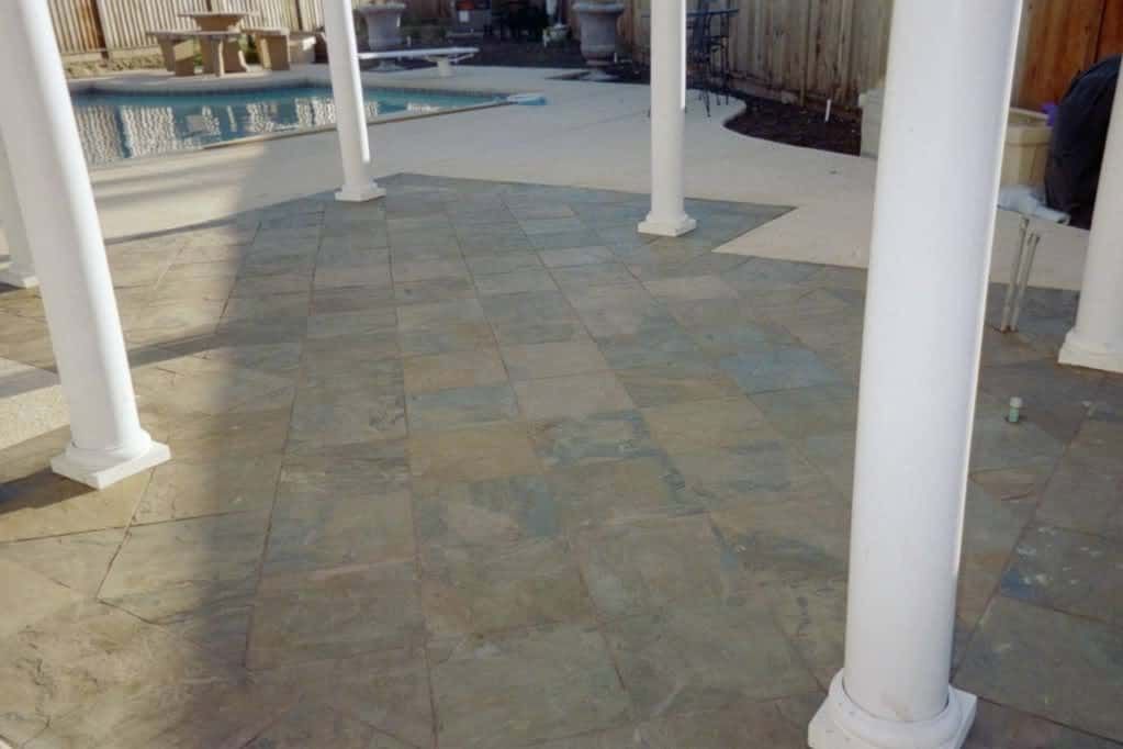 Stone tile patio floor beside pool with white columns