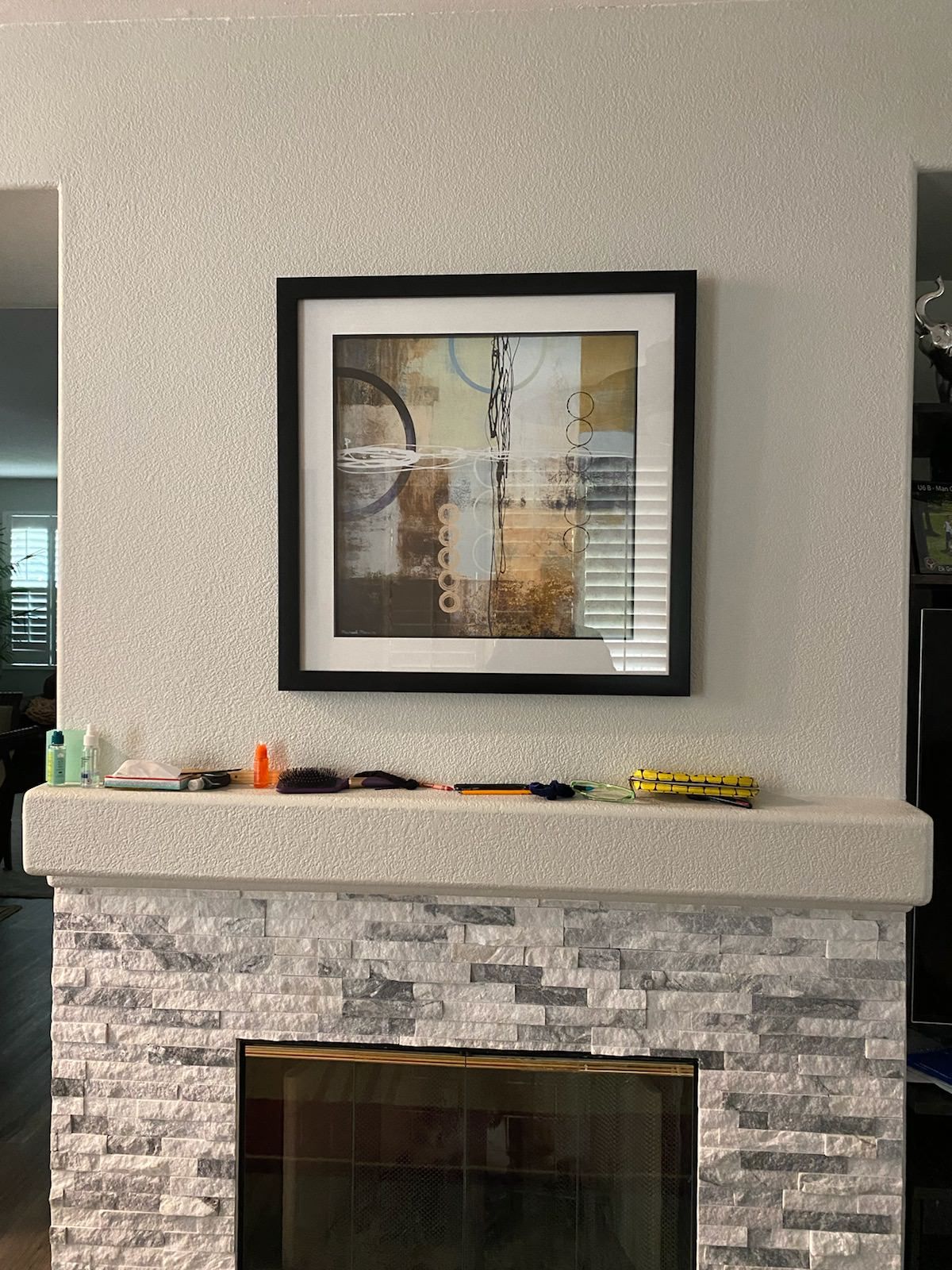 Stacked stone tile fireplace surround with white mantel and framed art above