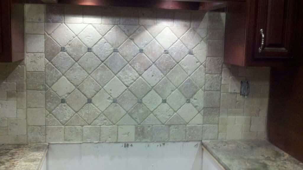 Diagonal stone tile backsplash with small square accents behind sink