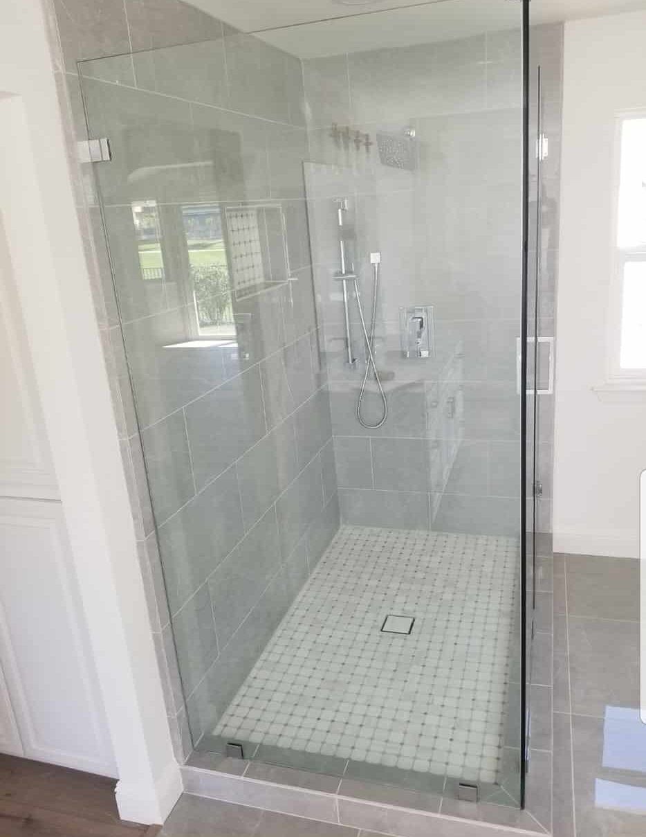 Glass-enclosed shower with gray tile walls and mosaic floor