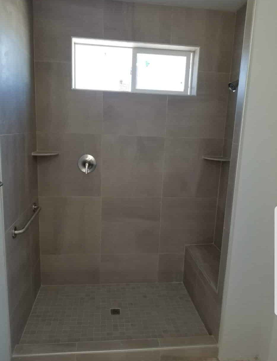 Tiled walk-in shower with bench, grab bar, and window