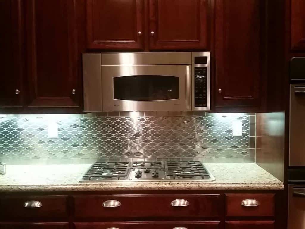 Stainless steel wavy tile backsplash above gas cooktop in kitchen